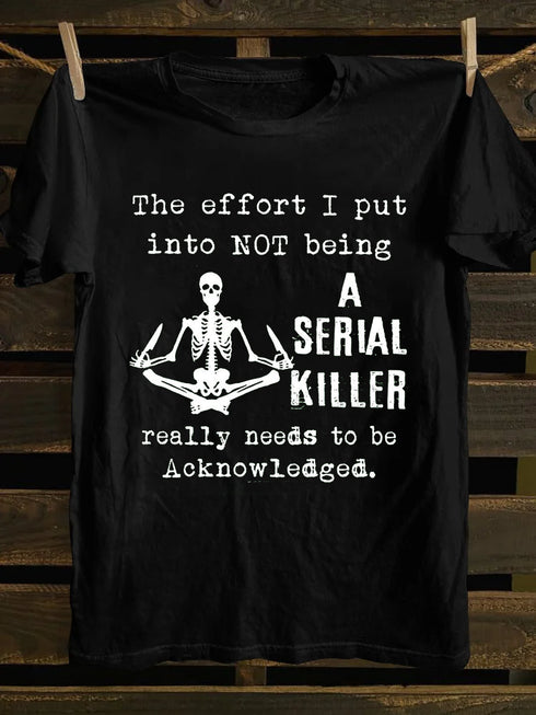 A black t-shirt with a graphic of a skull and the text 'THE EFFORT I PUT INTO NOT BEING A SERIAL KILLER REALLY NEEDS TO BE ACKNOWLEDGED.' displayed.